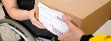 Close-up of deliveryman giving package to customer in wheelchair